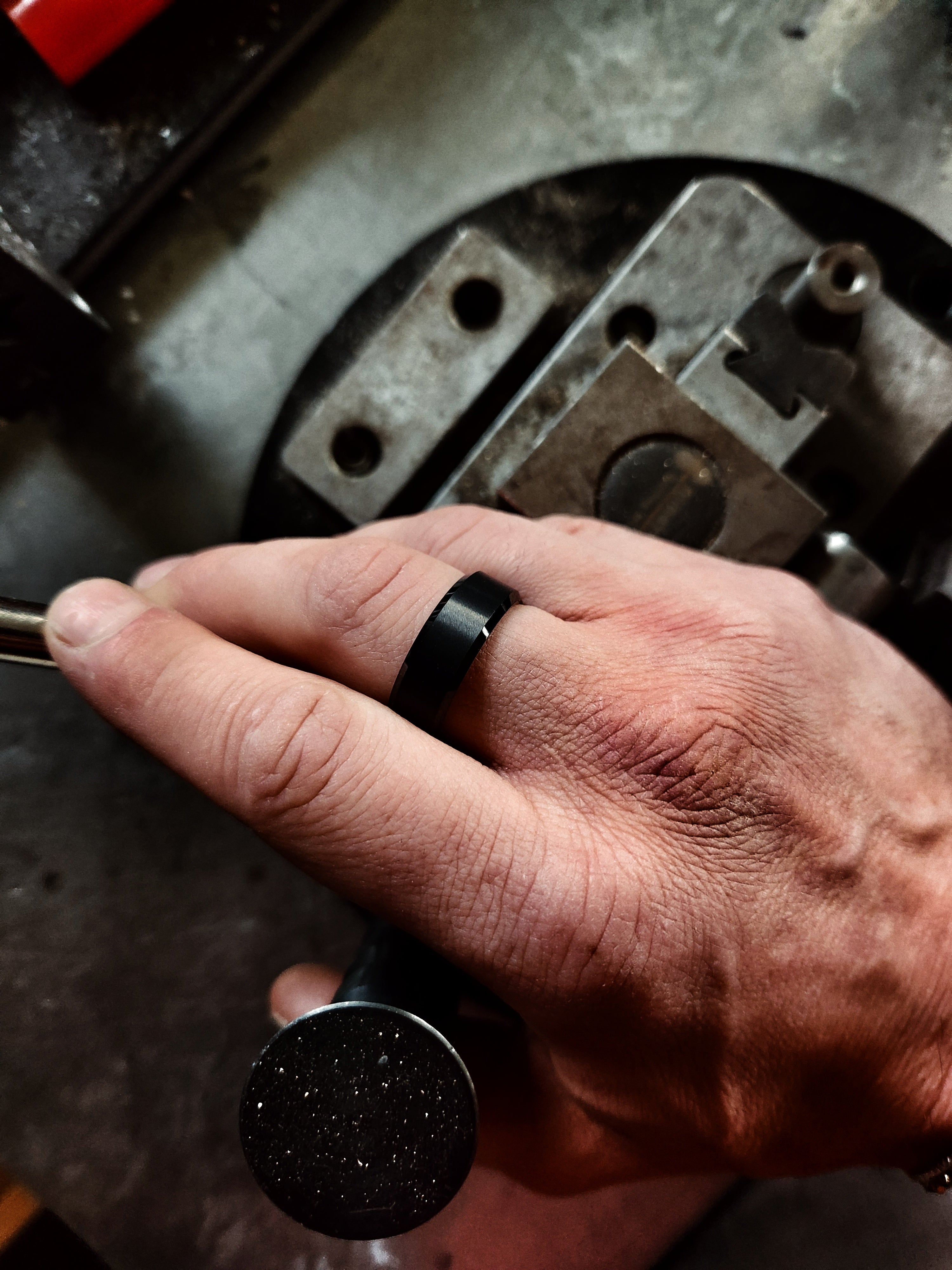 Men’s black beveled tungsten ring worn on hand in rugged workshop setting