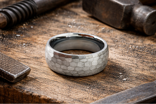 Men’s gunmetal tungsten ring with hammered matte finish in industrial workshop setting