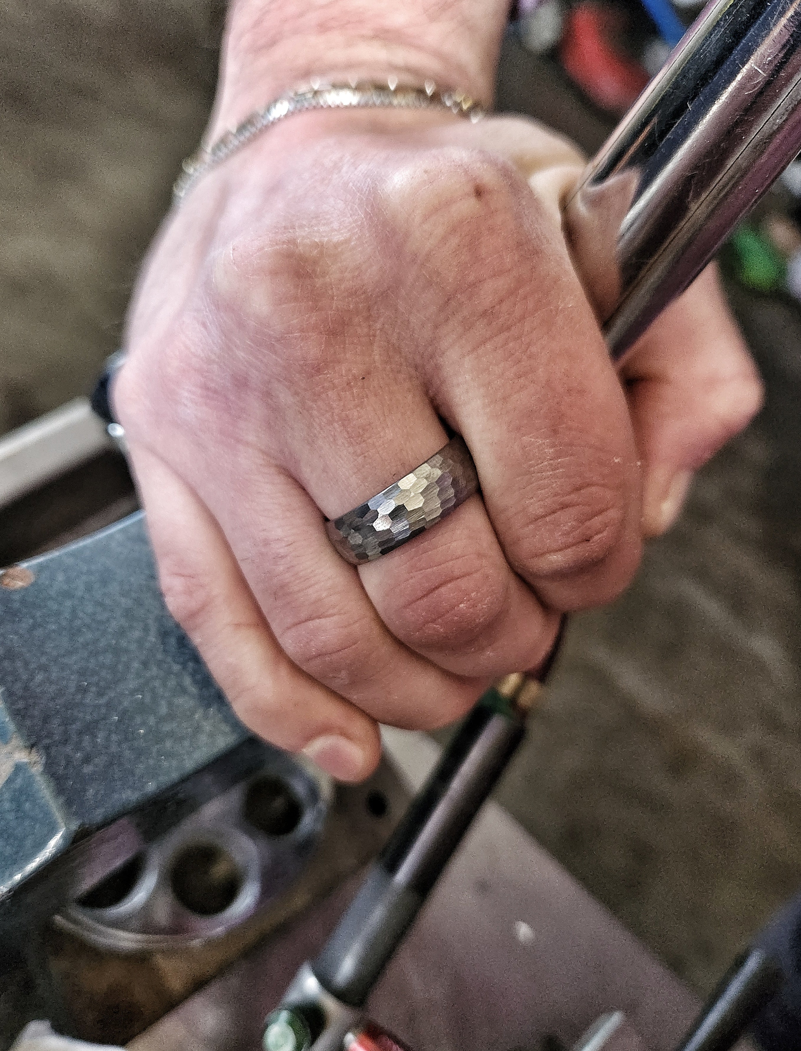 Men’s gunmetal hammered tungsten ring worn on hand in rugged workshop setting