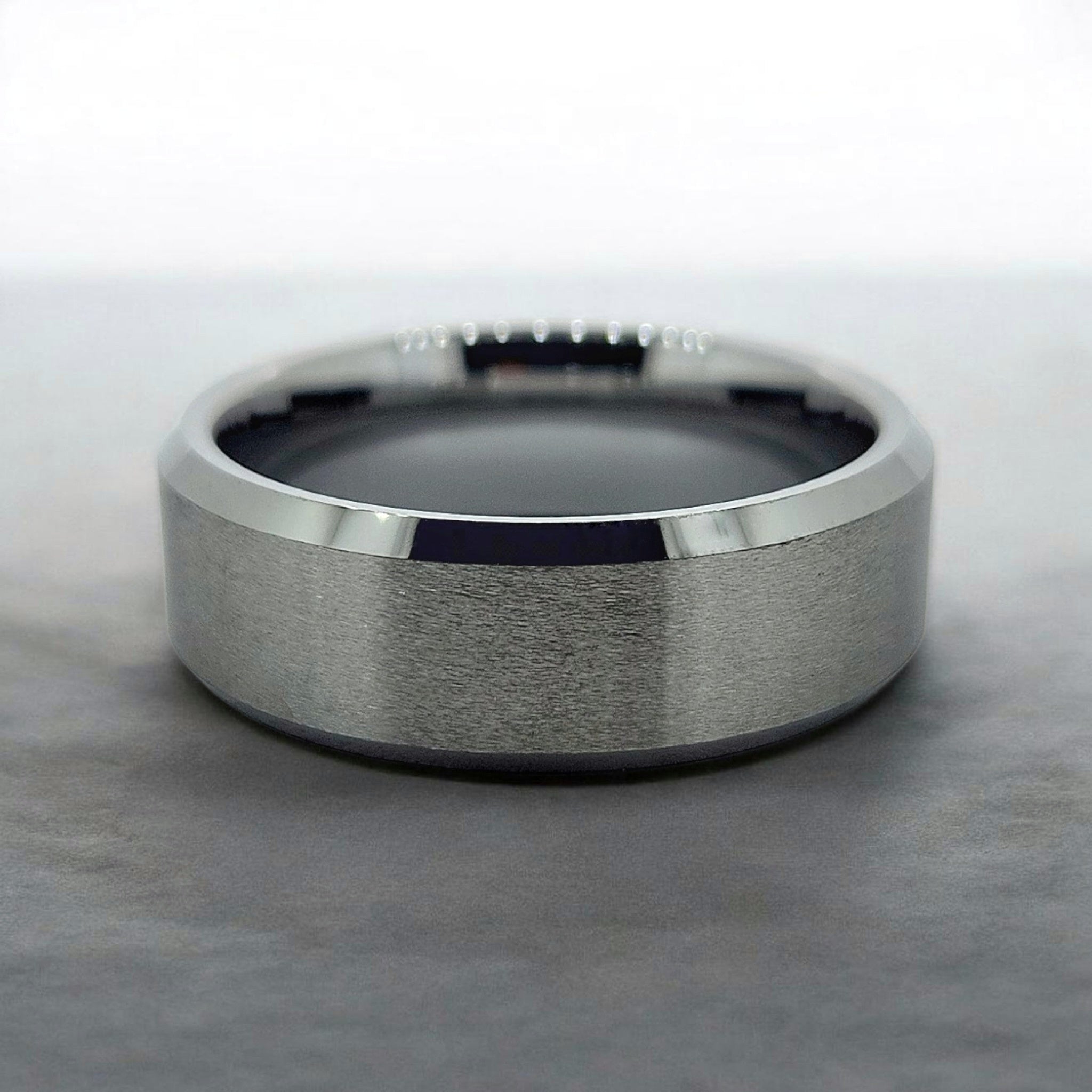 Silver domed tungsten ring with matte finish shown flat on industrial surface