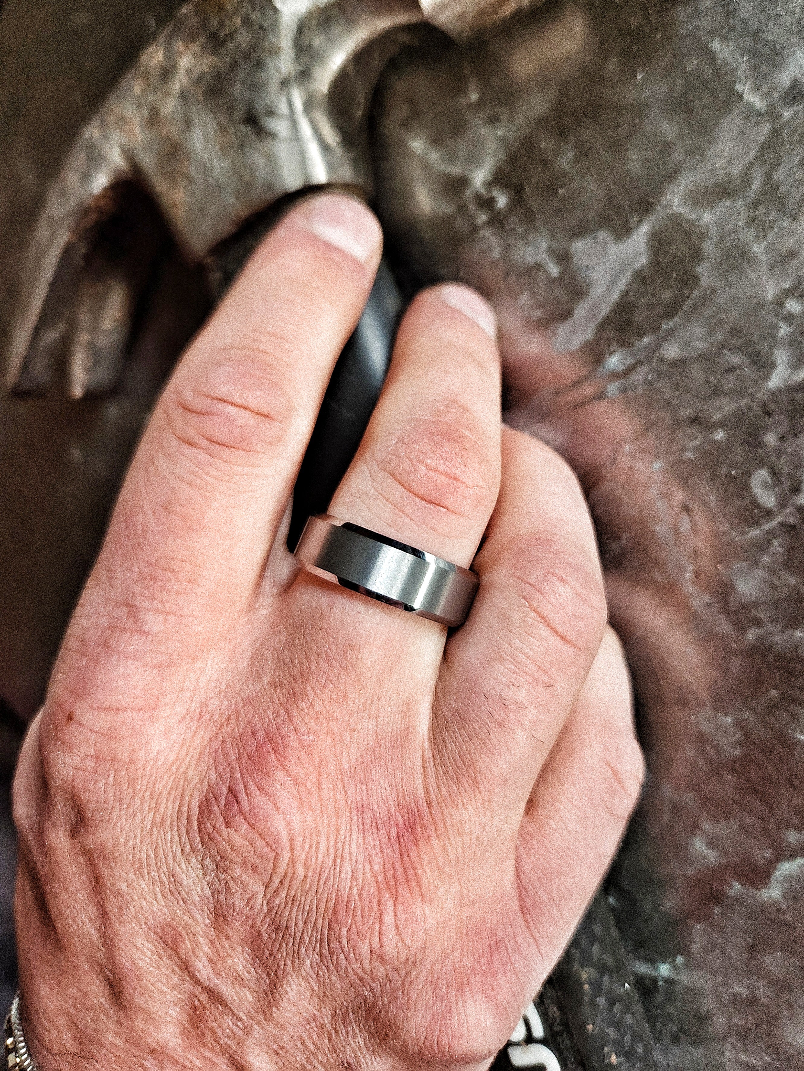 Men’s silver beveled tungsten ring worn on hand in rugged workshop setting