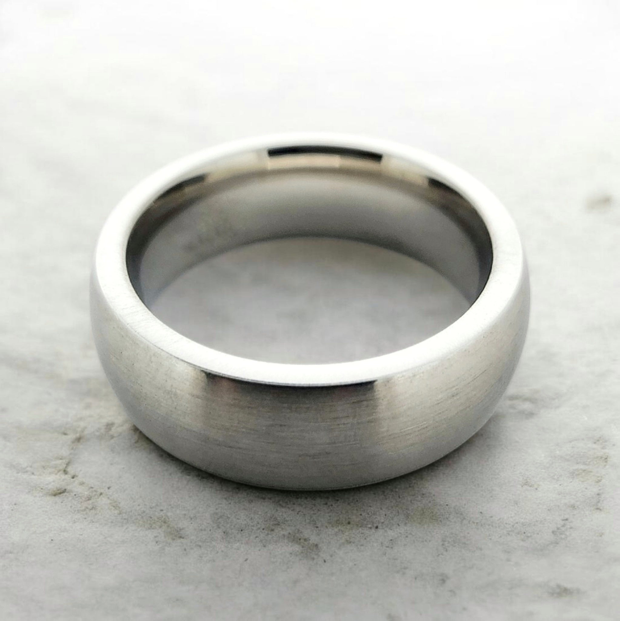 Silver domed tungsten ring with matte finish shown flat on industrial surface