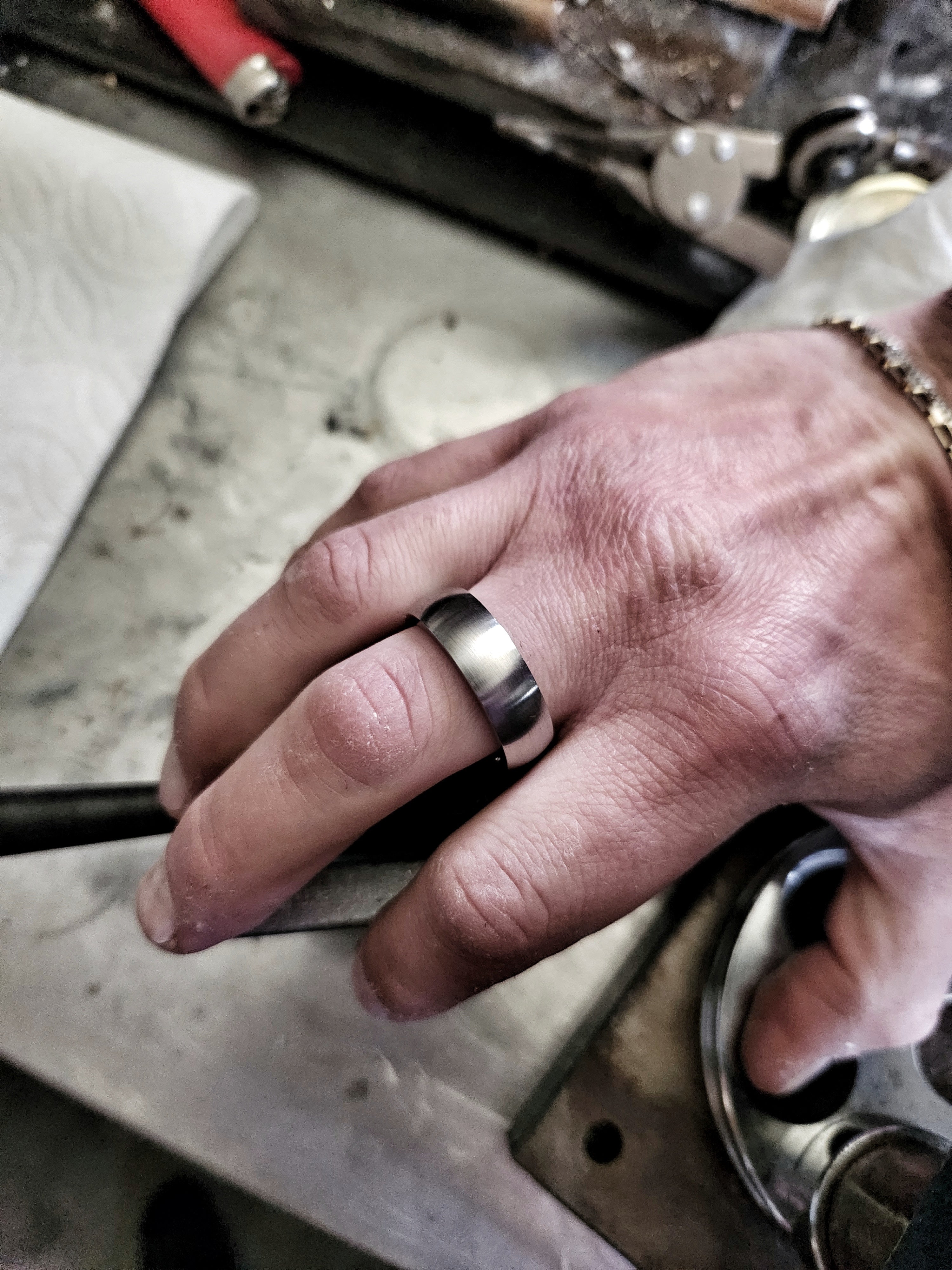 Men’s silver domed tungsten ring worn on hand in rugged workshop setting